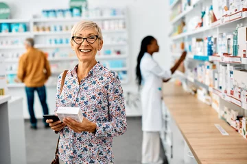 Fotobehang Happy senior woman buying medicine in pharmacy and looking at camera. © Drazen