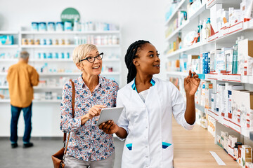 Young black pharmacist assists senior woman in buying medicine in pharmacy.