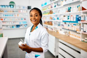 Happy African American pharmacist working in drugstore and looking at camera.