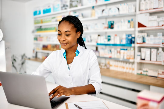 Young black pharmacist using laptop while working in pharmacy.
