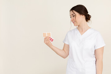 Side view of young attractive masseuse therapist woman wearing white uniform, holding and looking at beige cross tapes.