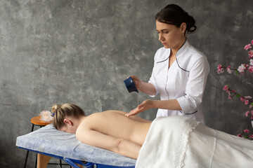 Portrait of serious middle-aged masseuse pouring massage aroma oil from blue plastic cup on bare...