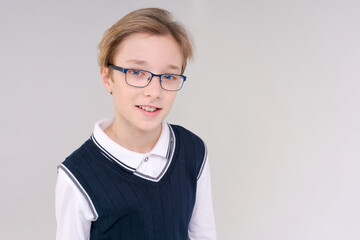 Shrugging caucasian boy, doubting shrugs, School boy, teenager with glasses in a white t-shirt. The boy chooses on a gray background.