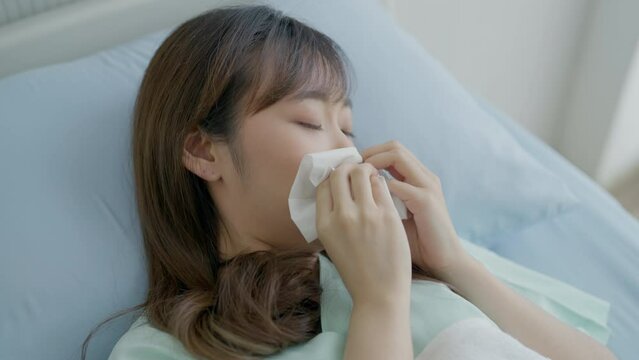 Asian woman sick and sneeze with tissue paper in the hospital. Woman with a cold blowing her runny nose with tissue. Healthcare and medical concept.
