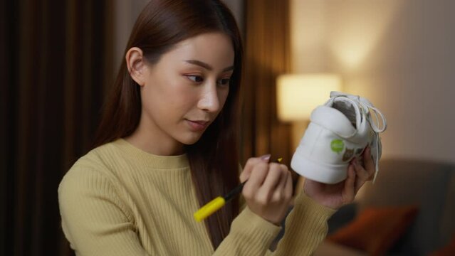 Asian female artist painting sneaker at home. Craftswoman painting on shoe near sewing patterns and devices in workshop.