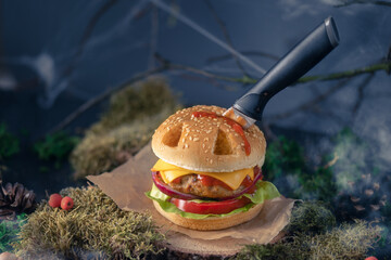 Halloween burger in a shape of pumpkin head jack lantern in a mystery forest. Scary cheeseburger on...