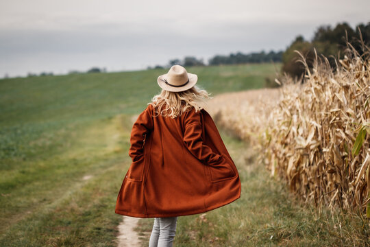 Happy woman with hat and red coat running at corn field. Fall season