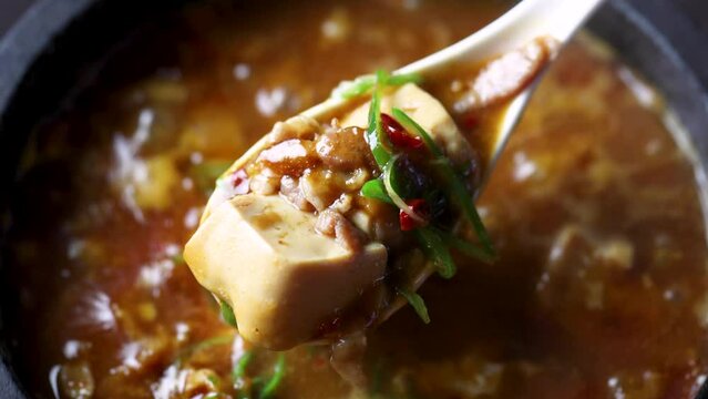 煮え立つ石鍋から豆腐を掬い上げ、とろとろで熱々な質感を閉じ込めた「麻婆豆腐動画」。レンゲから溢れる濃厚なルウの輝きが際立つシーンで、辛口メニューや本格中華の販促に最適な高品質素材です。 | Lifting sizzling hot Mapo Tofu with a spoon from a stone pot.