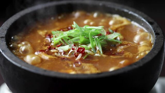 石鍋の中で煮立ち、気泡が上がる熱々の麻婆豆腐。赤黒いスープに豆腐、挽肉、刻みネギ、唐辛子が入り、湯気が立ち上がる様子を捉えたクローズアップ映像。飲食店メニュー、中華料理の紹介、レシピ解説、辛い料理やスタミナ料理をテーマにした広告や映像素材に。 | Close-up of boiling Mapo Tofu in a stone pot.