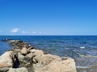 Coast of the Mediterranean Sea, waves, clear water, stone ridge against the blue sky with clouds boat with a yellow parachute.