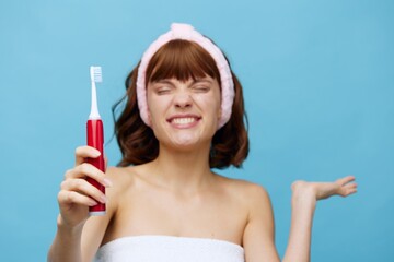 a young woman is standing in a white towel facing the camera, holding a red toothbrush in her hand...