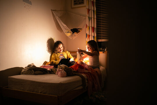 Silhouette shot of two smiling girls playing in the dark room on the bed
