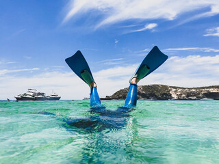 Snorkellers fins kicking above clear ocean  water with boats and coast in background