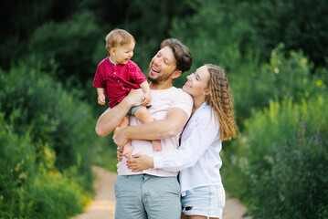 Fototapeta premium Happy and joyful family with a young son walks through the forest in the summer. Healthy lifestyle and happy parents