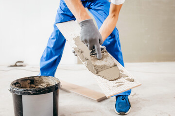 Repairman in grey gloves and special uniform laying cement on tile in a new house