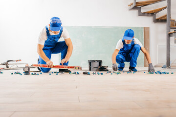Two workers in a special uniform laying tiles with tile leveling system and laser level on the floor in a new house