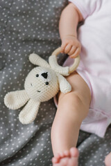 Soft knitted toy and a teether for teeth in the hands of a baby close-up