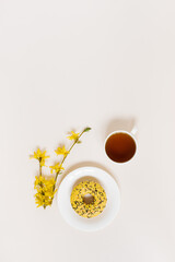 Fototapeta na wymiar Cup of tea and donut on a plate, yellow flowers. Tea break. Copy space and flat lay.