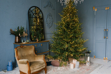 Christmas and New Year decorate the dark interior of the room. A festively decorated room with a fireplace, an armchair and a mirror. Festive Christmas night with lights on the Christmas tree