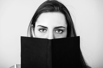 Leisure and hobbies concept. Portrait of beautiful woman with long dark hair reading book. Book with blank black old and aged cover and copy space. Model looking to camera. black and white image