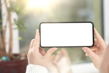 Woman watches video content or playing game on cell phone or mobile smartphone with white blank screen. mockup cellphone at home