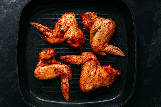 Raw chicken wings marinated in paprika and curry. Copy space. Raw meat on a grill pan. Dark background, top view.