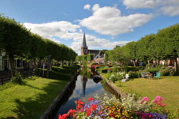 Eegracht canal surrounded by beautiful gardens in IJlst, Friesland, Netherlands, with Mauritiuskerk...