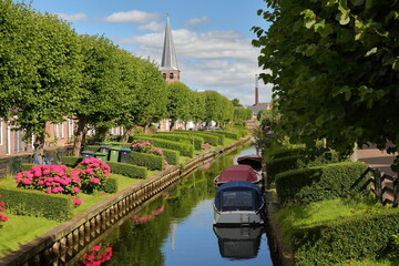 Eegracht canal surrounded by beautiful gardens in IJlst, Friesland, Netherlands, with Mauritiuskerk...