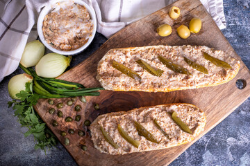 Sandwiches with rillettes, meat pate and pickled cucumber on a wooden cutting board, top view.