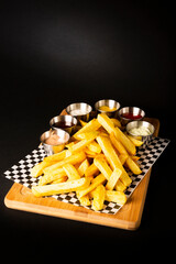 French fries on a wooden table accompanied by different types of sauces on a black background