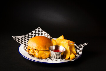 Two smashed hamburgers with cheese accompanied with french fries on a white plate over a black...