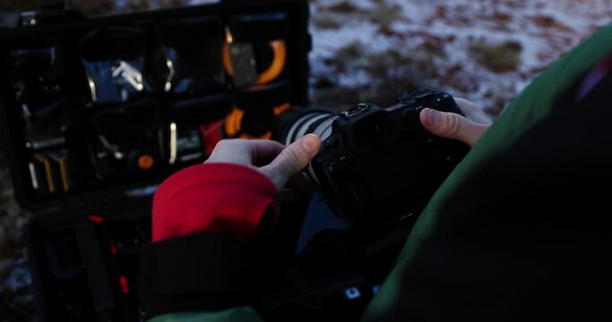 Guy setting up large DLSR camera with tele lens flipping screen, flight case with equipment, close up