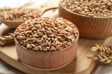 Fototapeta na wymiar Wheat grains in bowls on wooden board, closeup