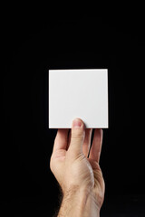 A man's hand holds a small paper white box on a black background.