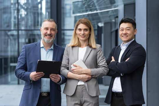 Successful dream team, diverse business group of asian man and business woman smiling and looking at camera, colleagues with crossed arms outside office building, professionals investors and bankers