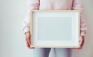 Woman holds a wooden frame with empty space. Mockup concept.