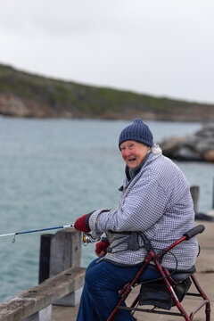 independent elderly lady sitting on wheely walker fishing rugged up in cold weather