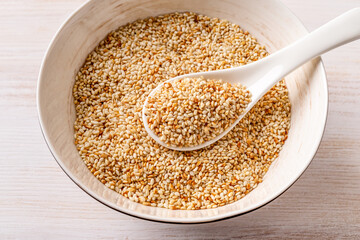 Toasted sesame seeds and white spoon in a porcelain bowl. Roasted organic benne grains closeup....