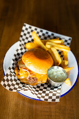Doble cheese burger with onion accompanied with french fries on a white plate on a wooden table