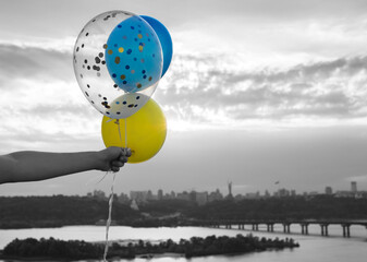 yellow and blue helium balloons in hand against sky and Dnieper river in Kyiv. color accent of flag...