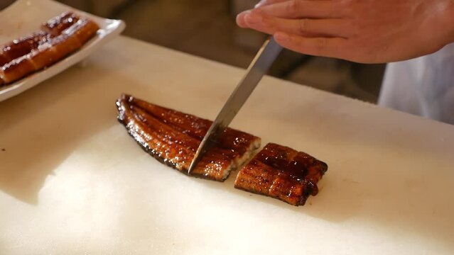 Hand Use Knife to Cut Japanese Grilled Eel into Pieces, Close Up