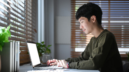 Fototapeta premium Focused young asian man freelancer searching information, checking email on laptop during remote working from home