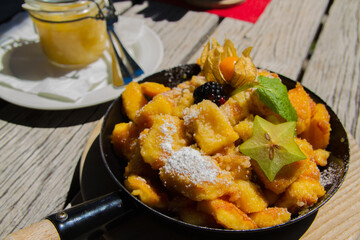 Traditional austrian dish Kaiserschmarrn with apple sauce and fruits on wooden table at Lech am Arlberg, austrian alps