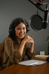 Asian woman podcaster wearing headphone recording podcast from home studio. Radio, podcasts,...