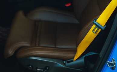 Automobile leather seat of a modern luxury car with a yellow safety belt. Yellow seat belt in a sports car close-up, blurry background. Brown leather car seat. Fasten your seat belts.