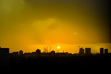Fototapeta na wymiar Golden sunset in the big city. Silhouettes of houses, industrial facilities - cooling towers, pipes, crane, houses and buildings of different heights. Beautiful sky, evening cityscape. Wallpaper