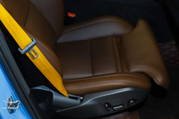 Automobile leather seat of a modern luxury car with a yellow safety belt. Yellow seat belt in a sports car close-up, blurry background. Brown leather car seat. Fasten your seat belts.