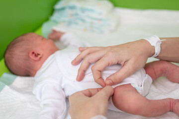 Obraz na płótnie Canvas The hands of a mother who has just given birth in the maternity hospital puts a bodysuit on her newborn baby after bathing and changing his diaper. newborn baby health care