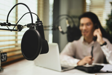 Professional microphone with man streaming his audio podcast in background. Entertainment, podcasts...