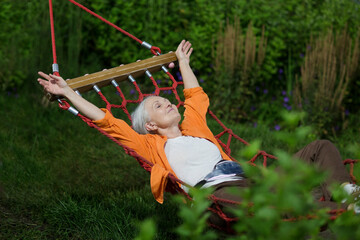 senior woman rests in a hammock in the summer evening in the garden